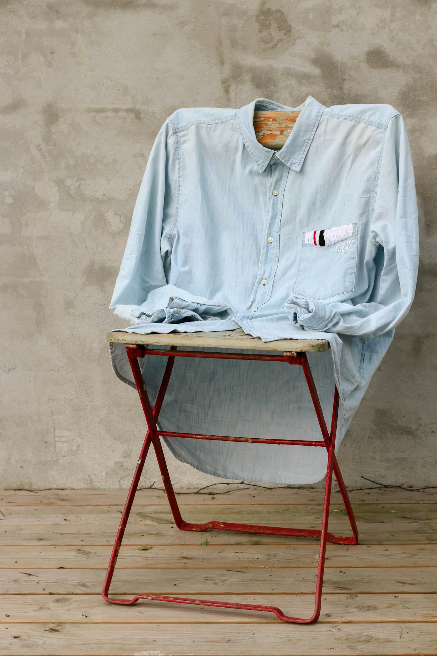 A pale blue shirt resting on a red folding chair